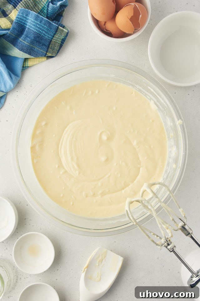 Overhead view of perfectly mixed, smooth lemon cheesecake batter in a glass mixing bowl.