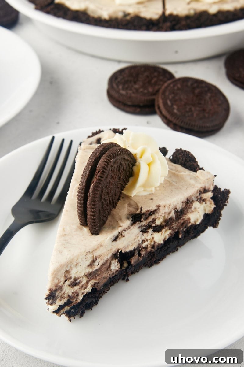 A perfect slice of No-Bake Oreo Pie on a white plate, with the remainder of the pie elegantly presented in the background.