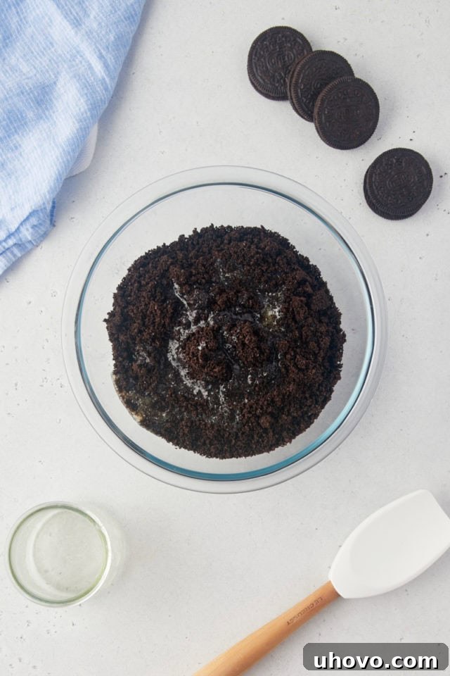 Overhead view of finely crushed Oreo cookie crumbs mixed with melted butter in a clear glass mixing bowl, forming the pie crust.
