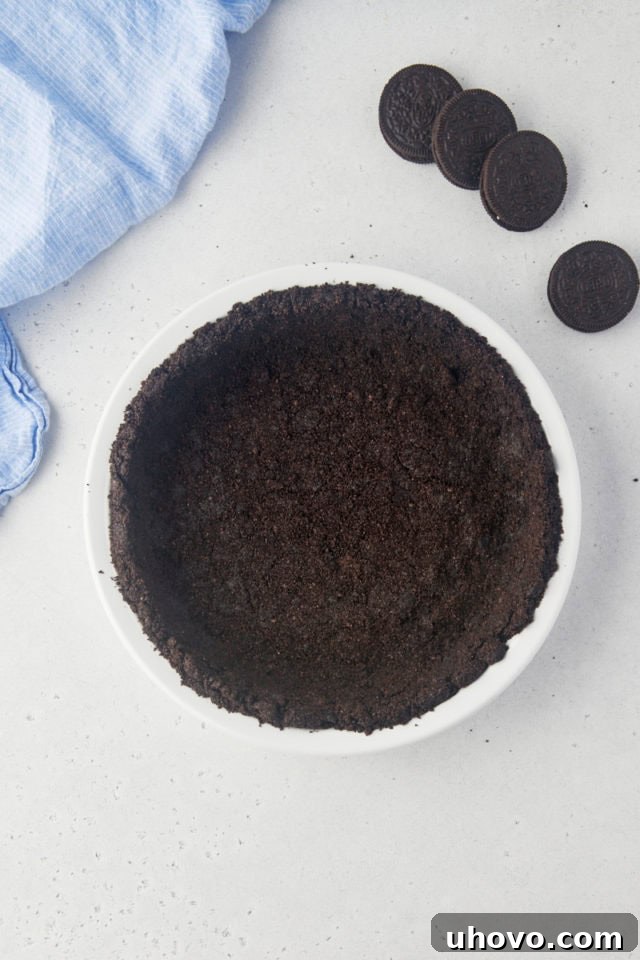 Overhead view of the rich, dark Oreo cookie crust expertly pressed into a 9-inch glass pie plate, ready for the filling.