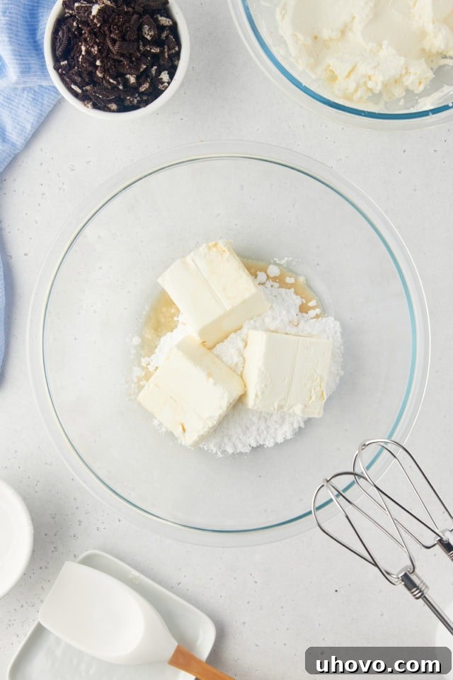 Overhead view of softened cream cheese, confectioners' sugar, and vanilla extract being mixed until completely smooth and creamy in a glass bowl.
