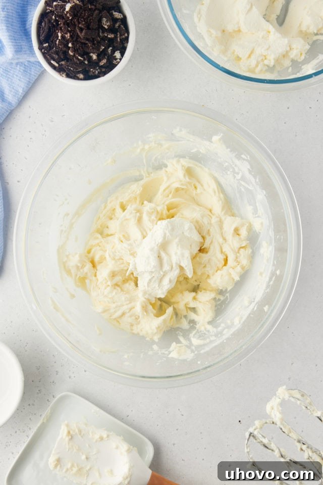 Overhead view of light, airy whipped cream being gently folded into the rich cream cheese mixture, creating the luscious filling for the Oreo pie.