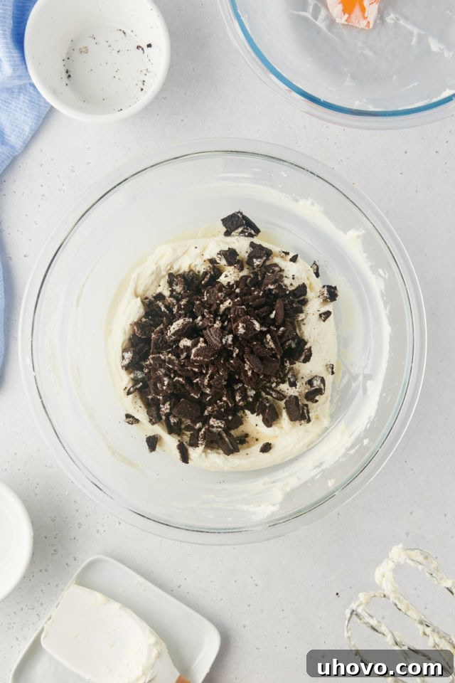 Overhead view of generously chopped Oreo cookies being added to the creamy pie filling, promising chunky cookie bites.