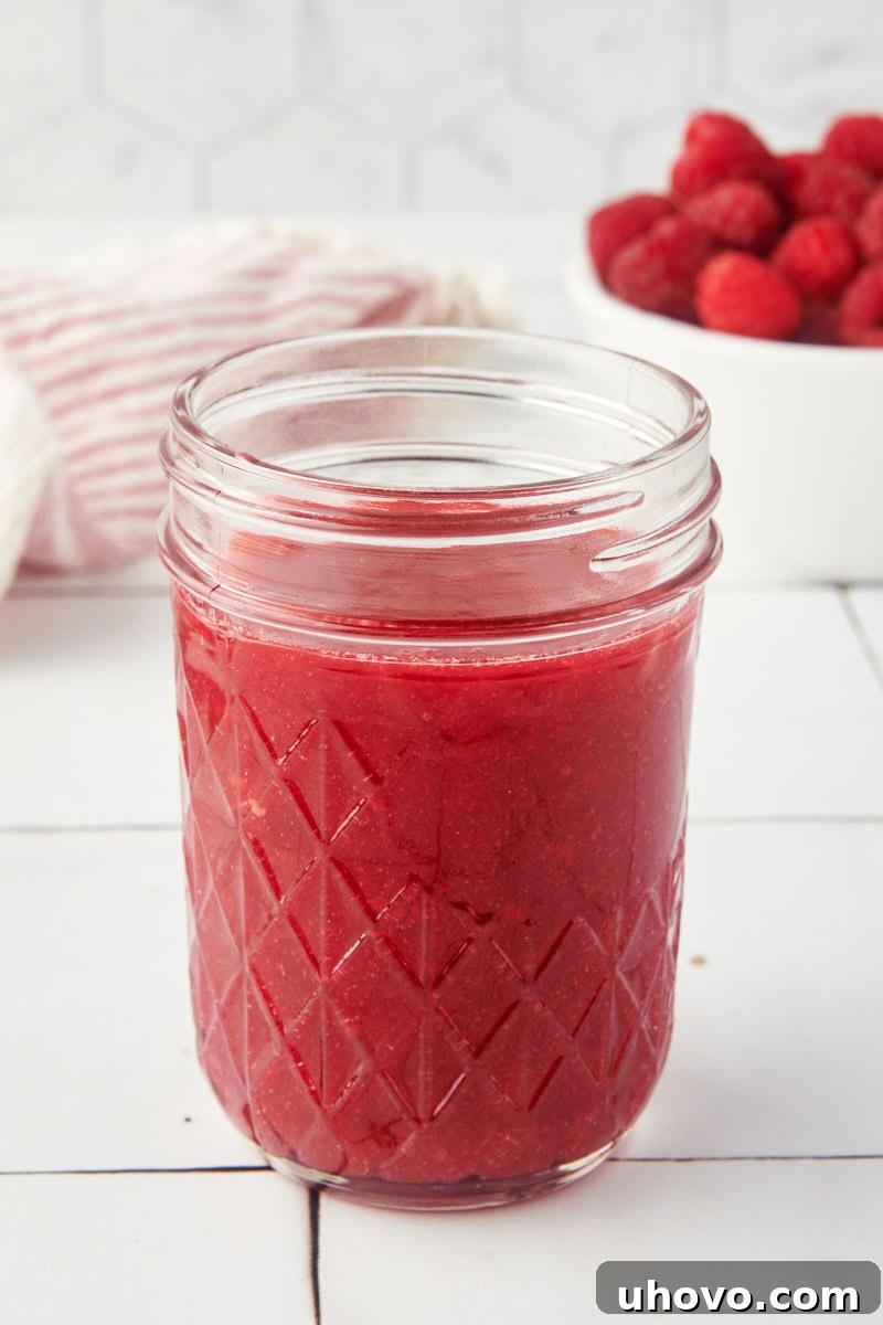A beautiful glass jar filled with vibrant homemade raspberry coulis, ready for use.