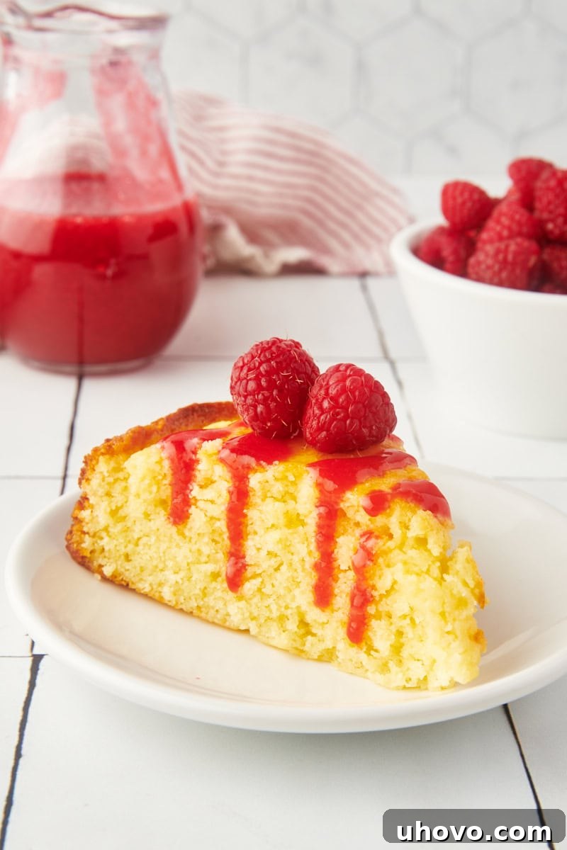 A slice of fluffy ricotta cake topped with generous raspberry coulis and fresh raspberries.