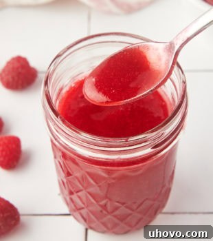 a jar of raspberry coulis with a spoonful held over the top