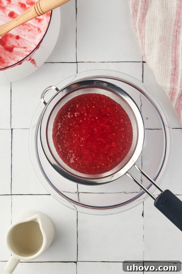 Overhead view of puréed raspberry coulis being poured into a fine-mesh sieve over a bowl.