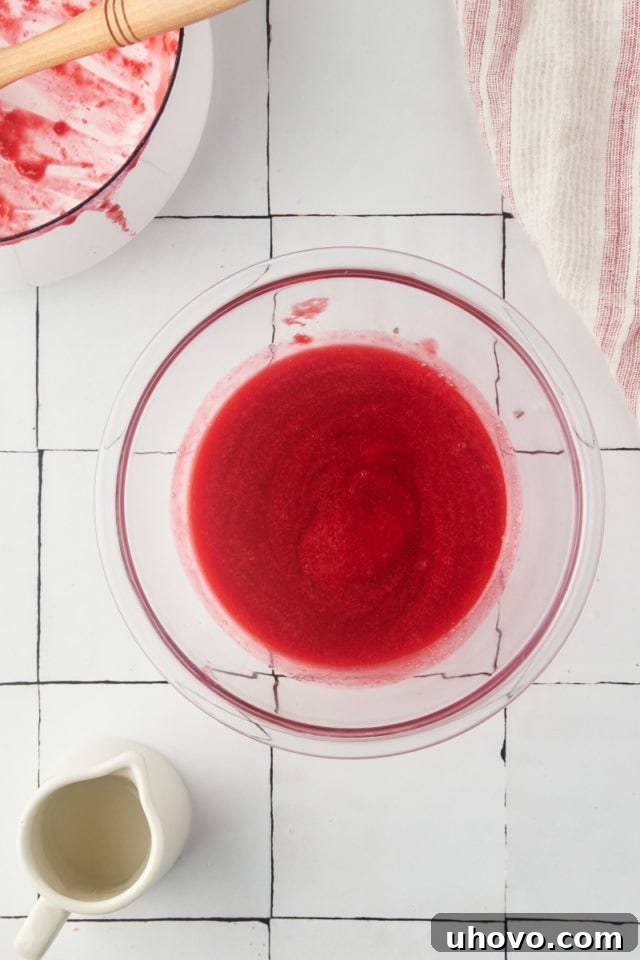 Overhead view of finished raspberry coulis in a clear glass bowl, showcasing its smooth texture and vibrant color.