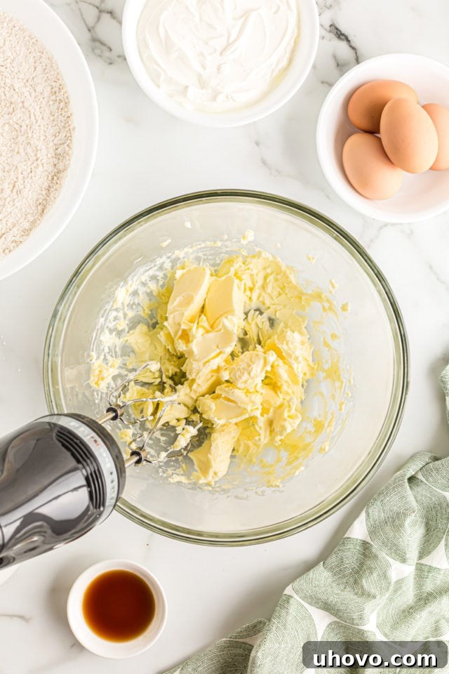 Overhead view of softened butter being beaten in a clear glass bowl with an electric mixer, preparing for the cake batter.