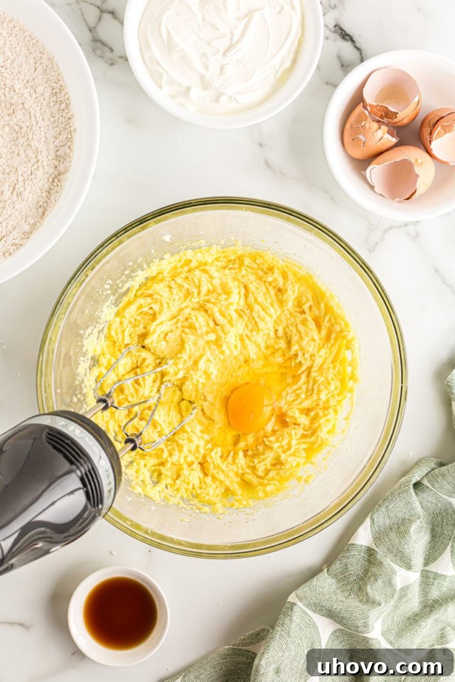 Overhead view of an electric mixer incorporating eggs one at a time into the creamy butter and sugar mixture for coffee cake batter.