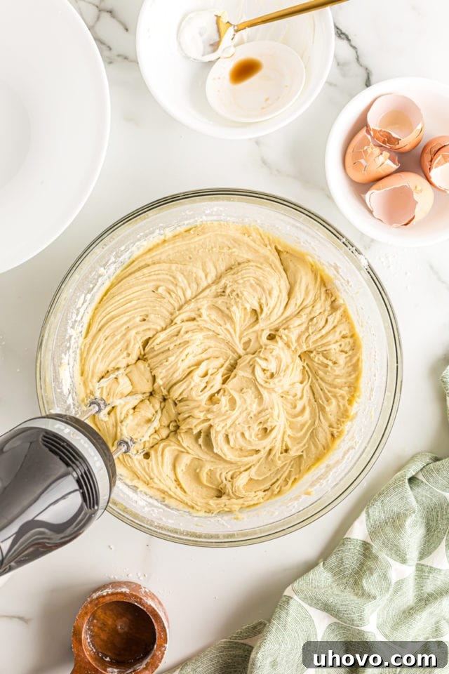 Overhead view of an electric mixer finishing the blending of all ingredients to form a smooth coffee cake batter in a glass bowl.