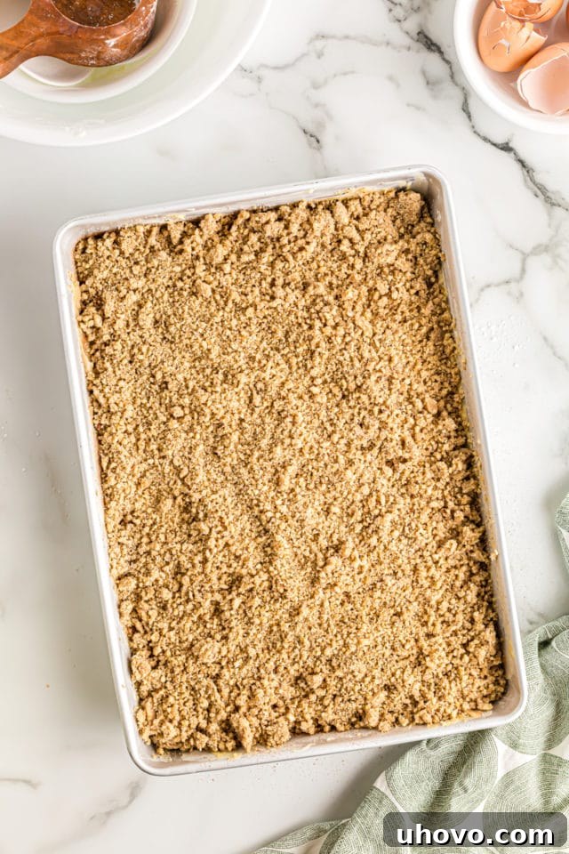 Overhead view of an unbaked sour cream coffee cake, beautifully layered with batter and swirl, and topped with the golden crumb mixture, ready for the oven.