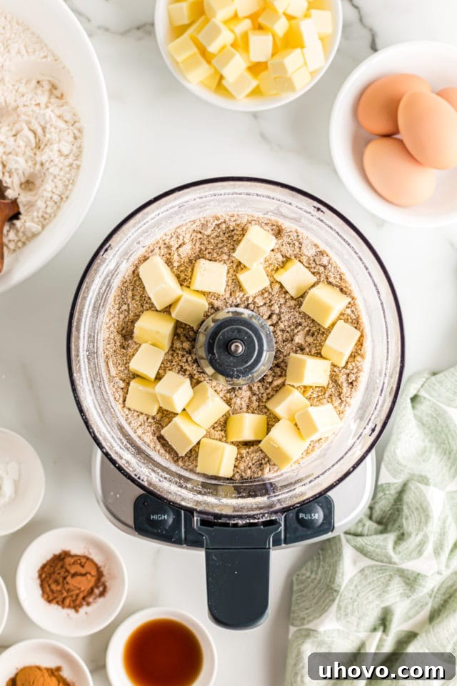Overhead view of cold butter cubes being added to the flour, sugar, and pecan mixture in a food processor for the crumb topping.
