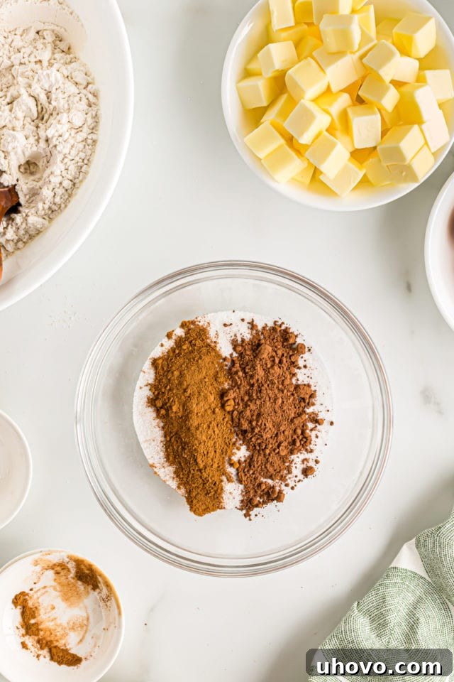 Overhead view of cocoa powder and cinnamon being added to granulated sugar in a clear glass bowl, preparing the swirl mixture.