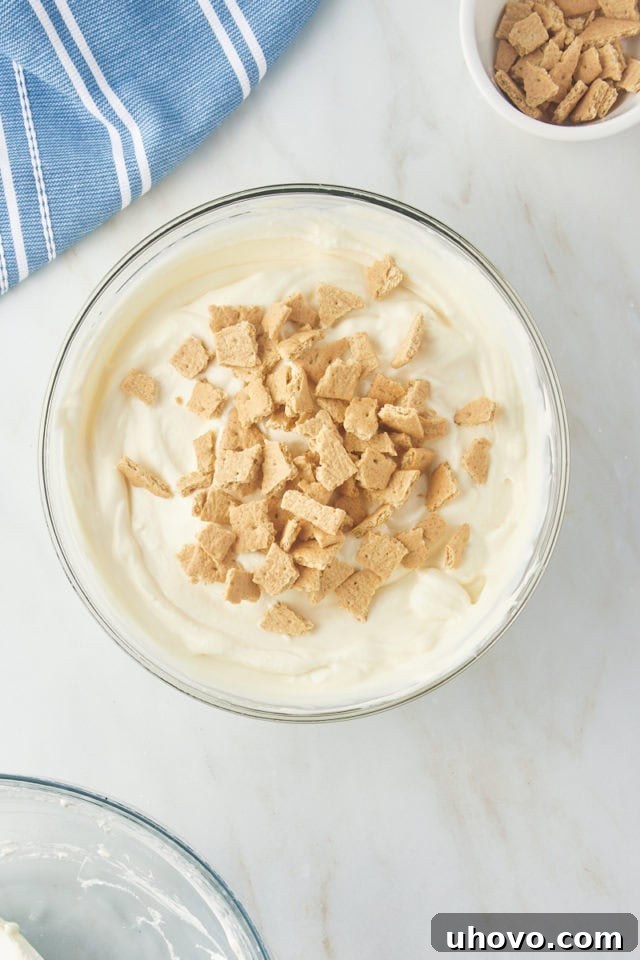 Crushed graham cracker pieces added to the completed no-churn ice cream base in a glass mixing bowl, ready for final folding.