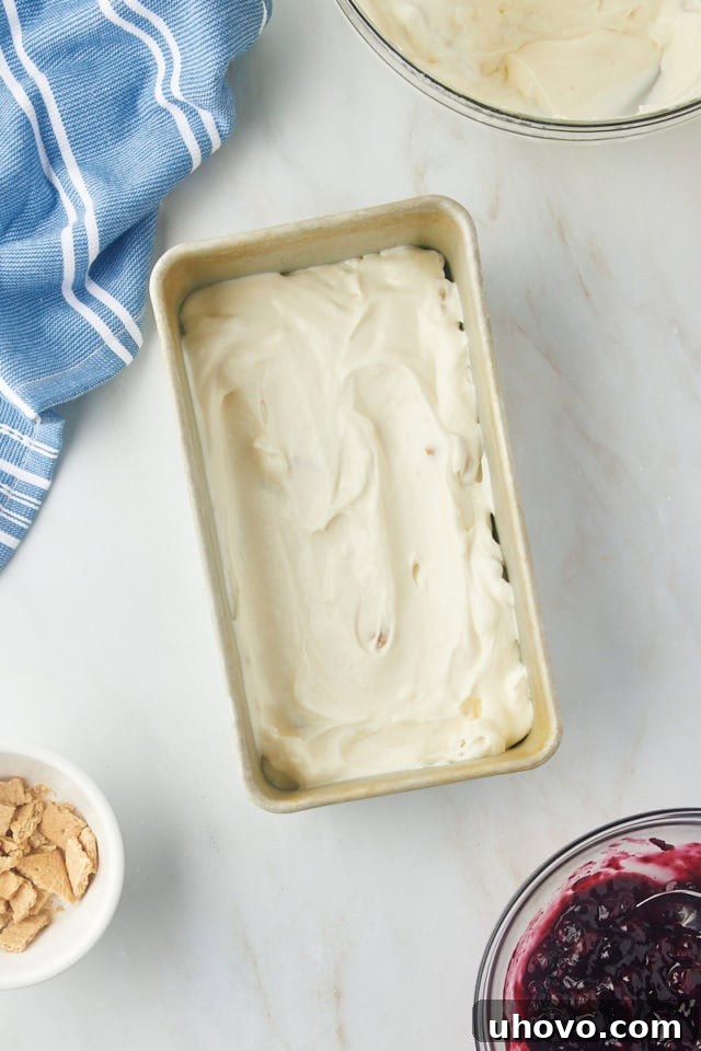 A layer of cheesecake ice cream base evenly spread in the bottom of a cold metal loaf pan.