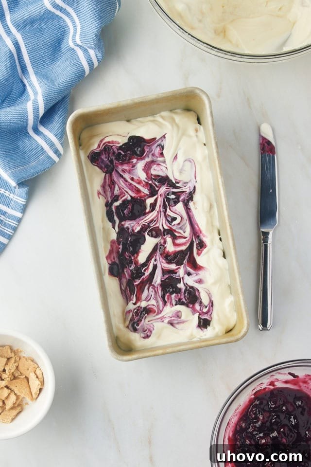 A thin knife or skewer gently swirling the blueberry compote into the cheesecake ice cream base to create marbling effect.