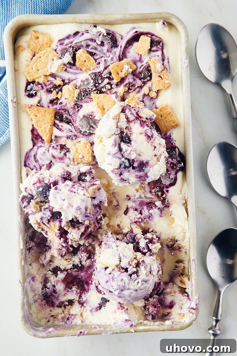 Multiple scoops of Blueberry Cheesecake Ice Cream piled high on top of the remaining ice cream in a metal loaf pan, ready to be served.