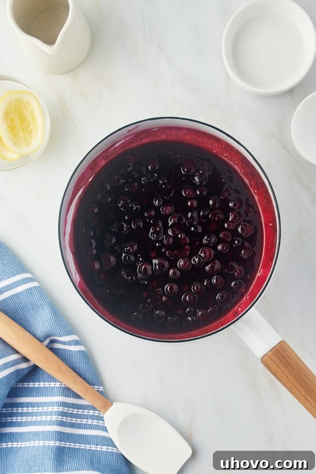 Thickened, cooked blueberry compote simmering in a white saucepan, showing burst berries and a rich purple color.
