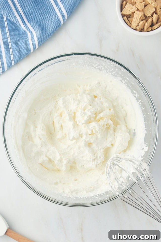 Fluffy, stiff peaks of whipped heavy cream in a clear glass mixing bowl, ready to be folded into the ice cream base.