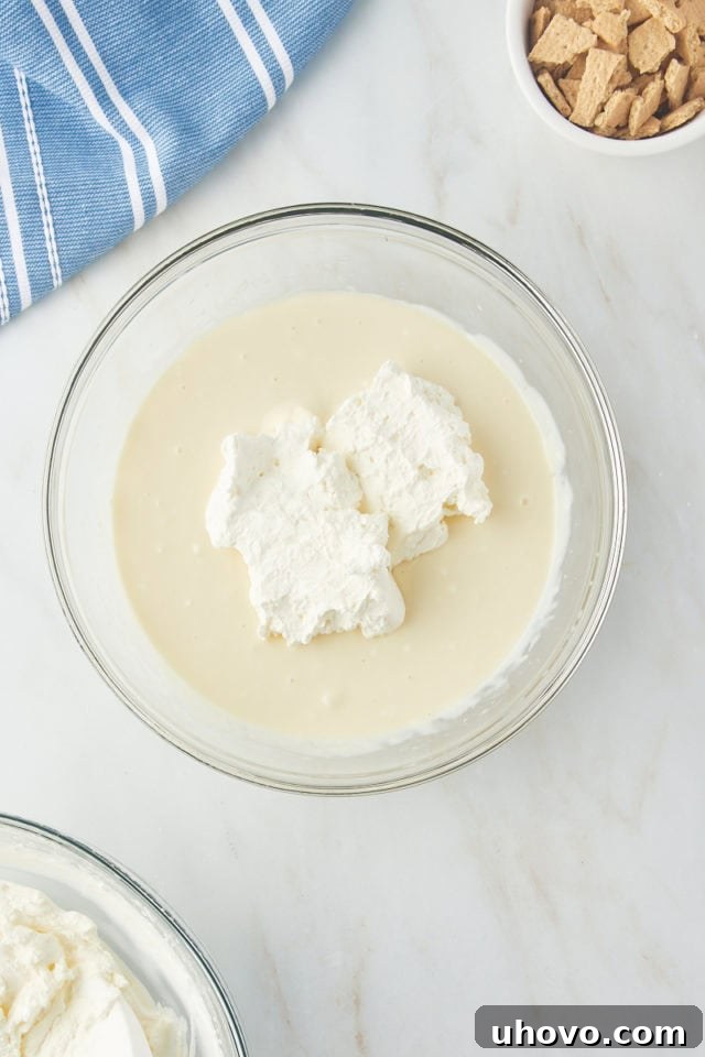 A quarter portion of whipped cream gently added to the cream cheese and condensed milk mixture in a glass bowl.