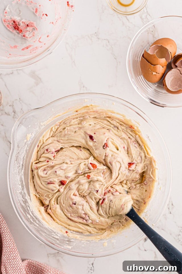 An overhead view of the strawberry pound cake batter in a glass mixing bowl, after the floured strawberries have been gently folded in, showing a well-combined and speckled mixture.