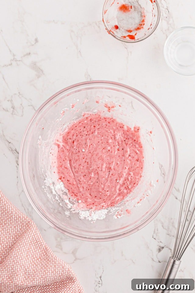 An overhead view of the smooth, vibrant pink strawberry glaze in a glass mixing bowl, freshly whisked and ready to be drizzled over the pound cake.
