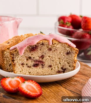 A partially sliced strawberry pound cake topped with a vibrant strawberry glaze, elegantly served on a white plate.