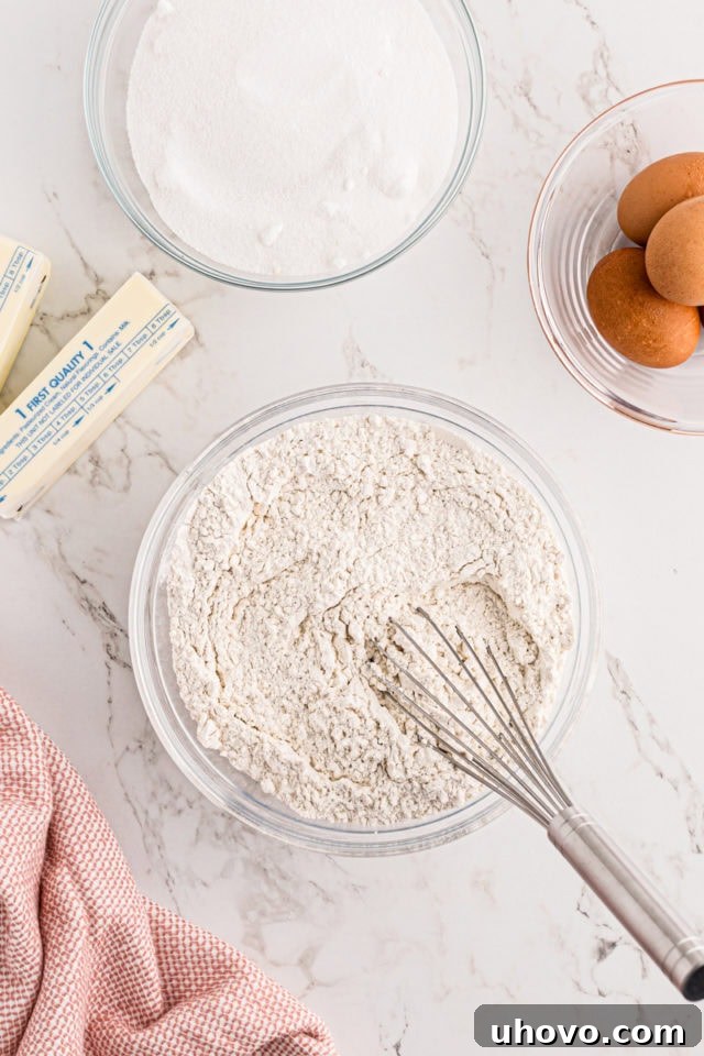An overhead view of a bowl containing perfectly measured dry ingredients for strawberry pound cake, including flour, baking powder, baking soda, and salt, ready to be whisked.