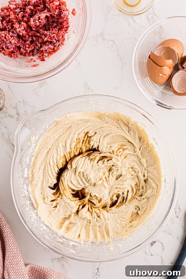 Vanilla extract being drizzled into the strawberry pound cake batter in a glass mixing bowl, indicating the final flavoring step before adding fruit.