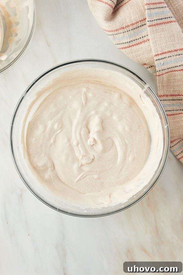 Overhead view of the whipped cream being gently folded into the cinnamon condensed milk mixture in a mixing bowl