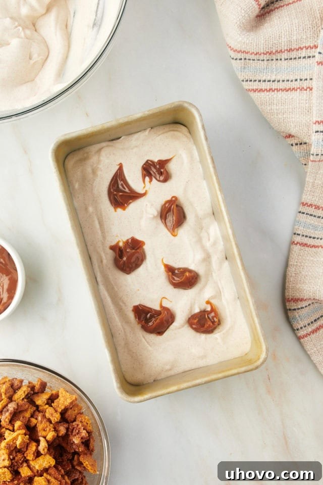 Overhead view of the first layer of ice cream mixture being added to a loaf pan, with dollops of dulce de leche on top