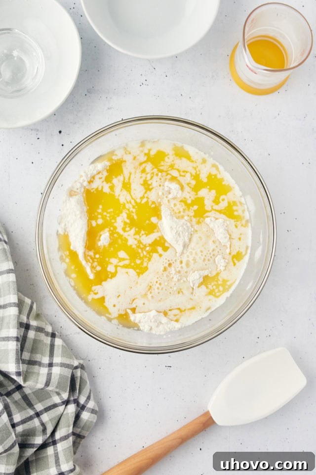 Melted butter and milk being poured into the dry ingredients mixture in a glass mixing bowl, to form the rich, wet batter for the cobbler topping.