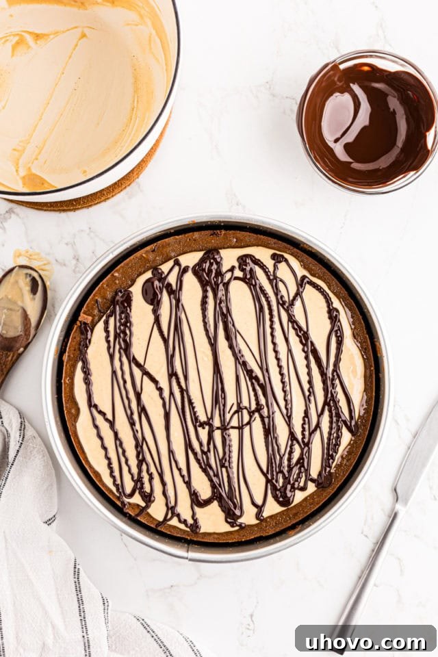 Dark chocolate being artfully drizzled over the peanut butter topping of the chocolate peanut butter cheesecake.
