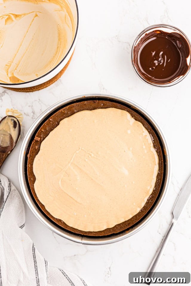 The smooth peanut butter and white chocolate topping being spread evenly over the chilled chocolate peanut butter cheesecake.