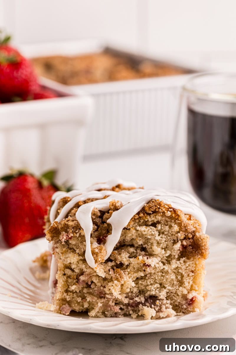 a slice of strawberry coffee cake on a white plate with berries and more cake in the background