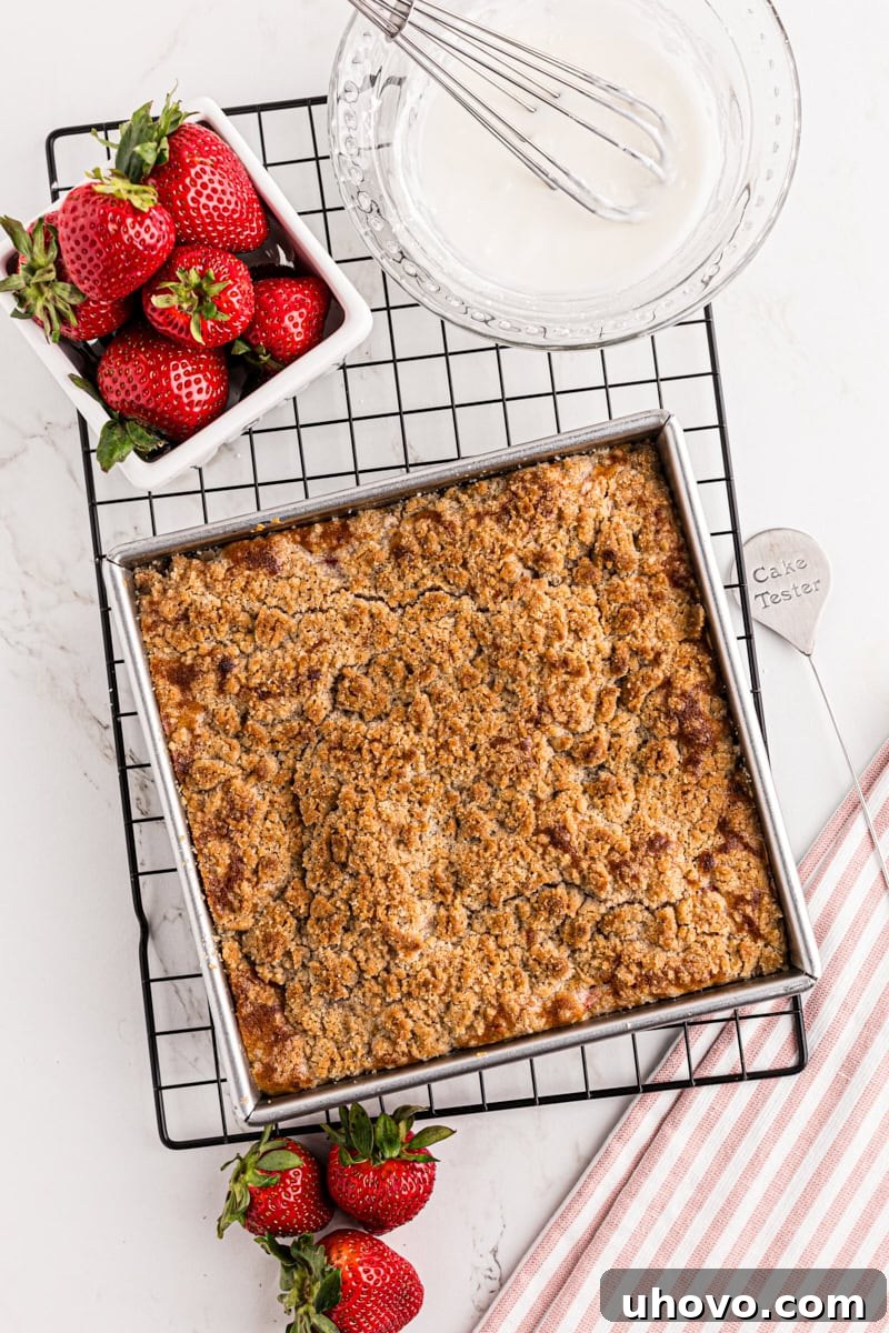 overhead view of freshly baked strawberry coffee cake on a wire rack with strawberries and freshly mixed glaze alongside