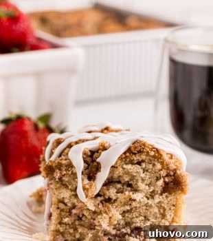 a slice of strawberry coffee cake on a white plate with berries and more cake in the background