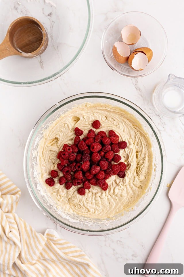 Overhead view of fresh raspberries gently folded into cake batter in a glass mixing bowl.