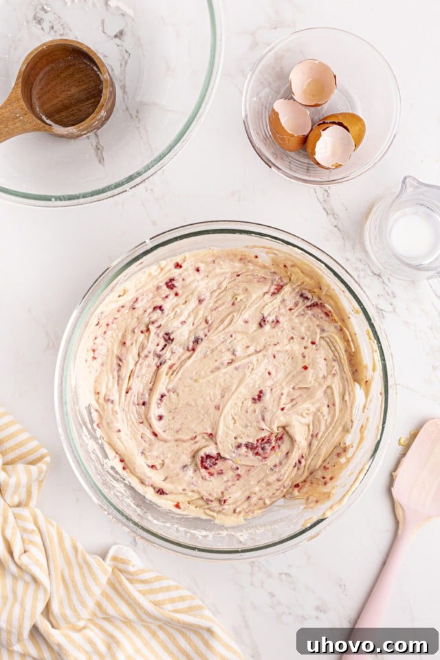 Overhead view of mixed lemon raspberry cake batter in a glass mixing bowl, with raspberries evenly distributed.