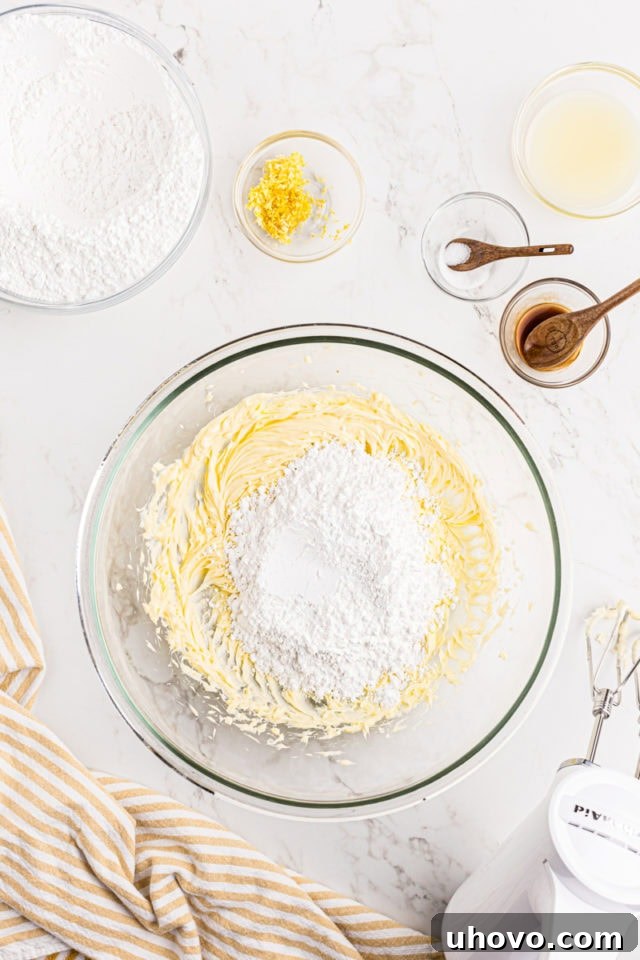 Overhead view of confectioners' sugar being gradually added to the creamed butter in a glass mixing bowl.