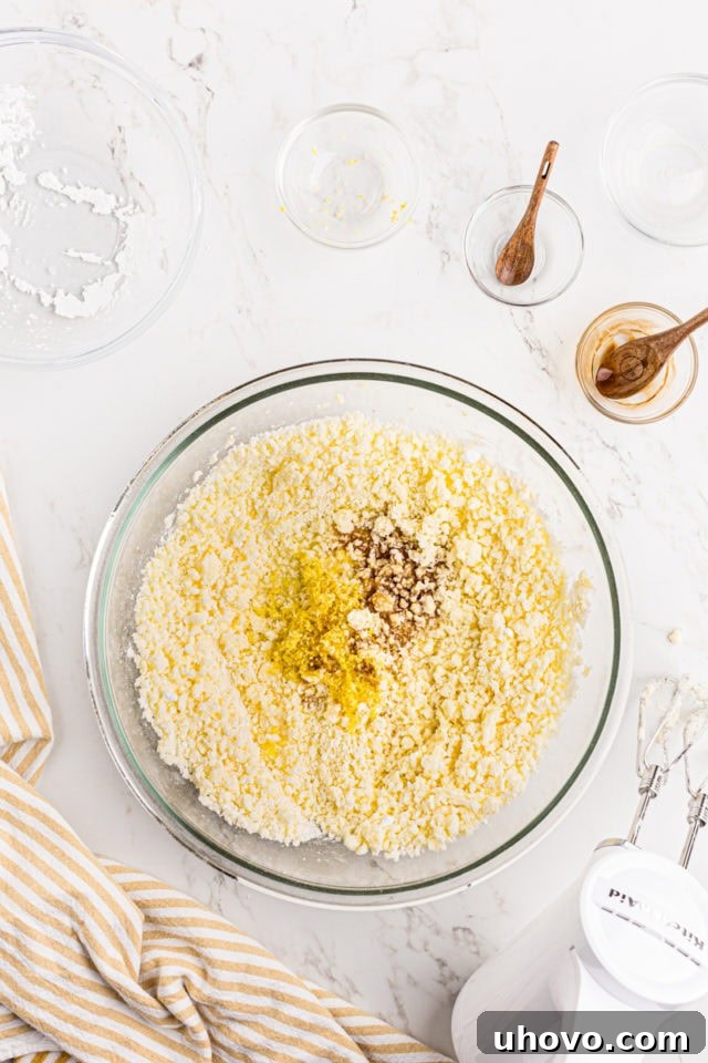 Overhead view of vanilla extract, lemon juice, and lemon zest being added to the frosting mixture.