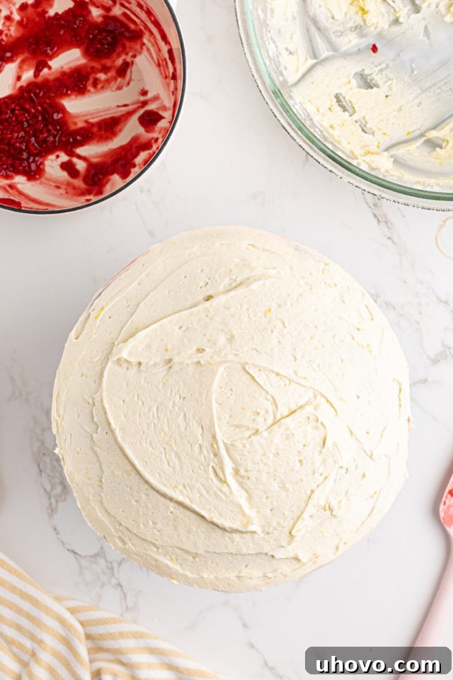 Overhead view of a fully frosted lemon raspberry cake, with a smooth and even layer of lemon frosting.
