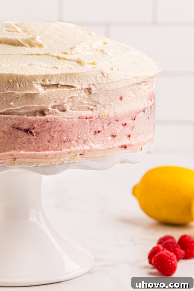 A partial view of a fully decorated lemon raspberry cake, with vibrant yellow frosting and hints of red berries, sitting on a white cake stand.