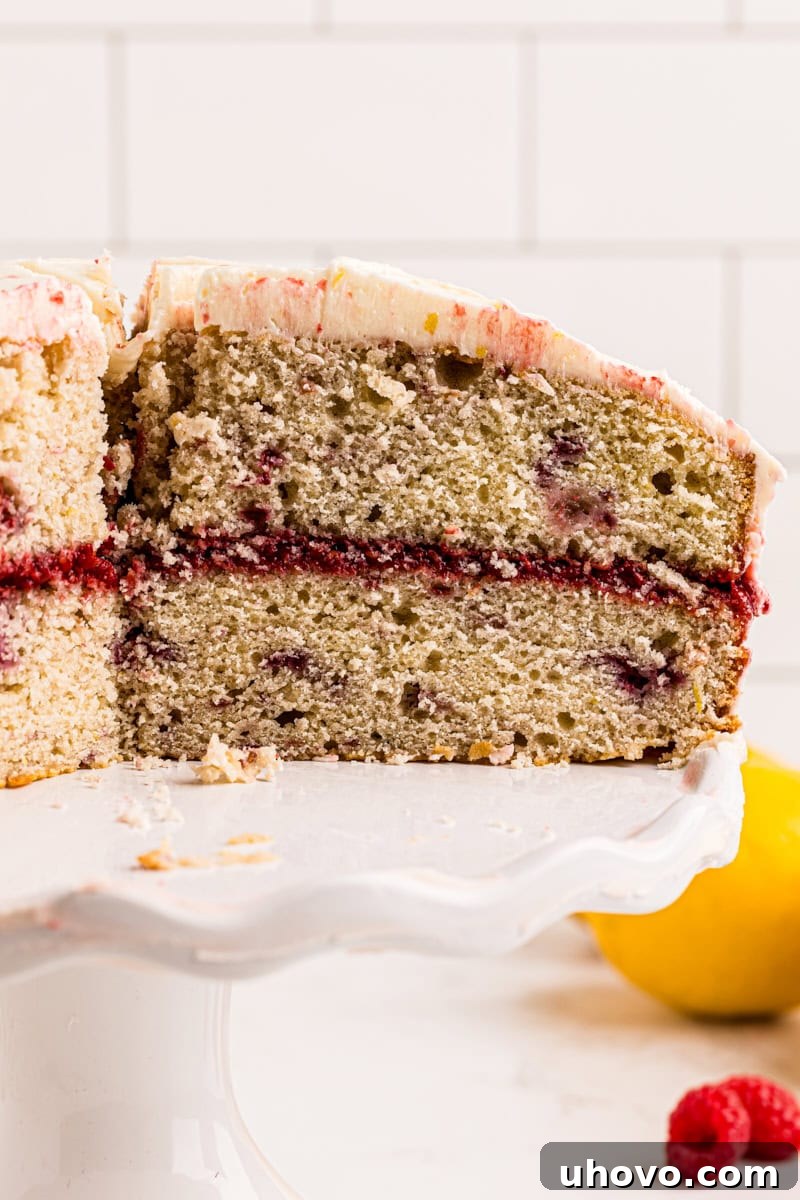 A partially sliced lemon raspberry cake on a white cake stand, showcasing its beautiful layers of cake, filling, and frosting.