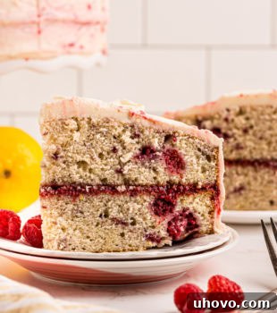 Side view of a slice of lemon raspberry cake on a white plate, showcasing its layers.