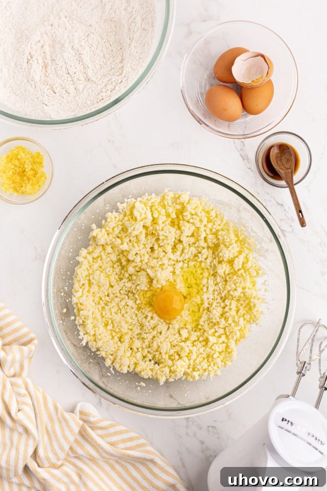 Overhead view of an egg being added to the creamed butter and sugar mixture in a glass bowl.