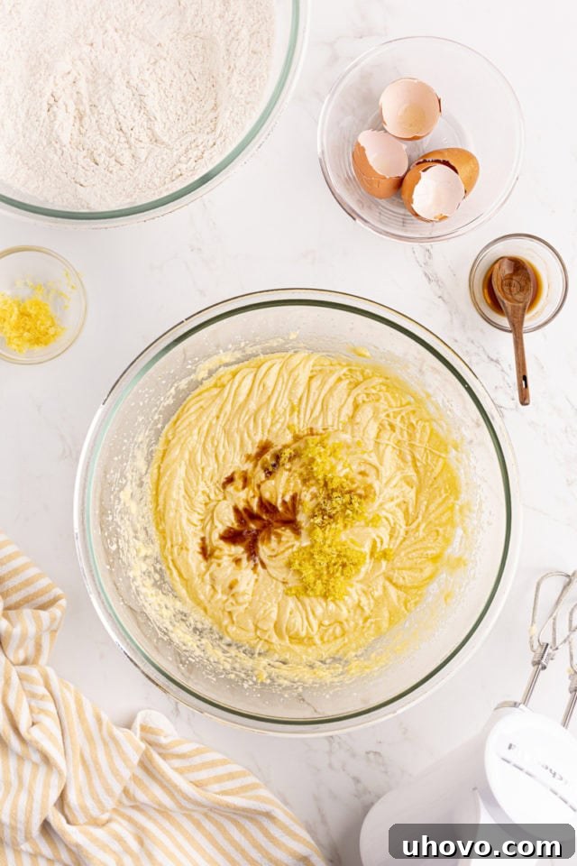 Overhead view of vanilla extract and fresh lemon zest being added to the cake batter in a glass mixing bowl.