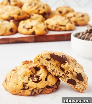 Half of a thick chocolate chip cookie leaned against another cookie with a tray of cookies in the background, showcasing the gooey interior.