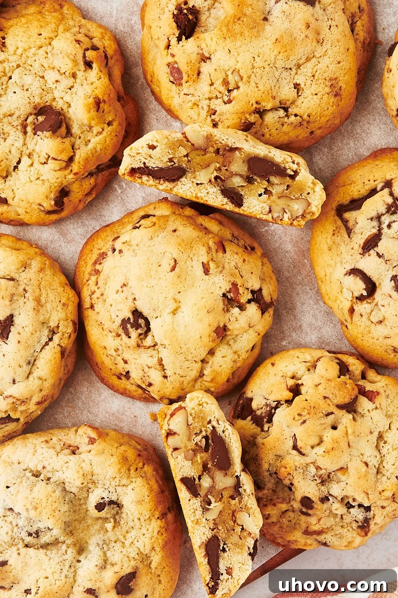 Overhead view of several thick chocolate chip cookies on parchment paper, with some broken to reveal their gooey, chocolate-filled centers.